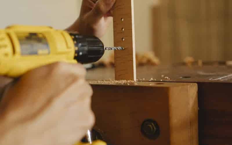 Crop anonymous skillful male using screwdriver while drilling holes in timber detail in workshop