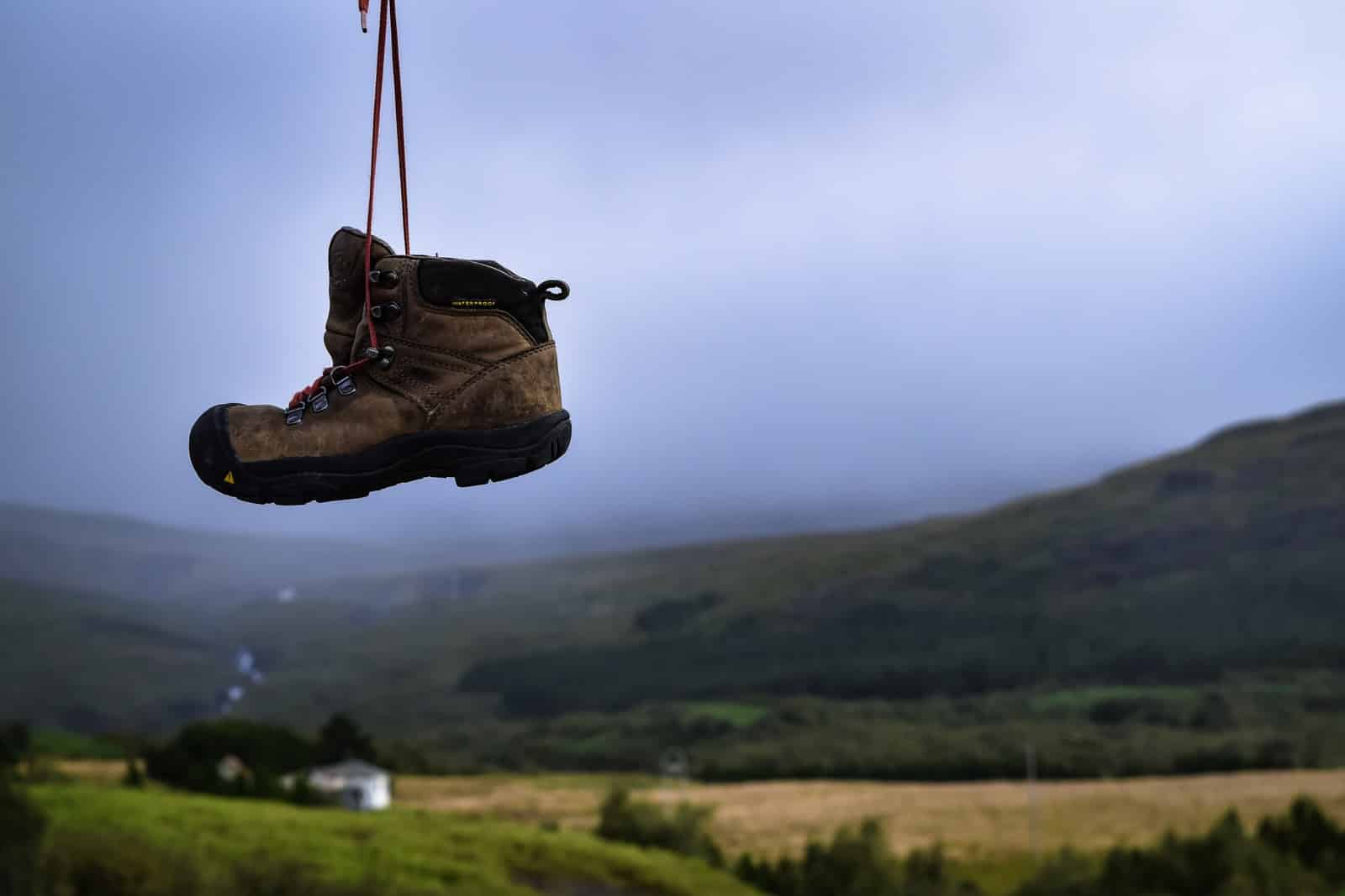 brown and black boot hanging overlooking mountain and field view during daytime